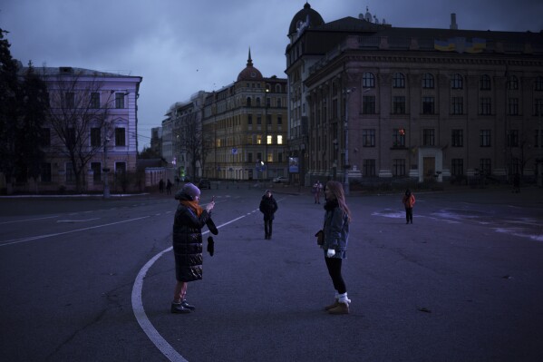 People walk and take photos on a street closed for cars at dusk in Kyiv, Ukraine, Sunday, Nov. 26, 2023. (AP Photo/Felipe Dana)