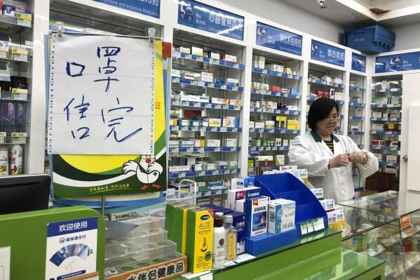 Pharmacist Liu Zhuzhen stands near a sign reading "face masks are sold out" at her pharmacy in Shanghai, Tuesday, Jan. 21, 2020. Heightened precautions were being taken in China and elsewhere Tuesday as governments strove to control the outbreak of a novel coronavirus that threatens to grow during the Lunar New Year travel rush. (AP Photo/Fu Ting)