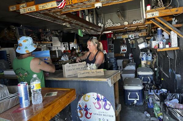 Ashley Galassi, a bartender at Tina’s, a watering hole at Fisherman’s Wharf in Fort Myers, Florida, attends to a patron on Friday, Oct. 7, 2022. She says the bar will likely be demolished and reopen elsewhere. Hurricane Ian might have come and gone, but it has done long-term damage to the small businesses of a region heavily dependent on tourists and seasonal residents.  (AP Photo/Bobby Caina Calvan)