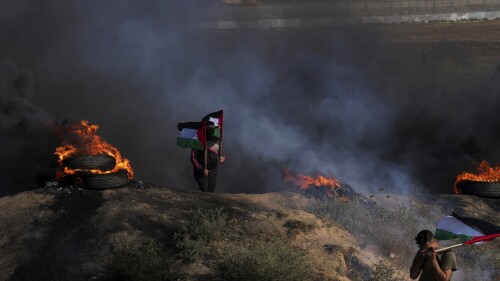 Pengunjuk rasa Palestina mengibarkan bendera nasional mereka ketika yang lain membakar ban selama demonstrasi menentang serangan militer Israel di kota Jenin, Tepi Barat, di sepanjang perbatasan dengan Israel, di sebelah timur Kota Gaza, Senin, 3 Juli 2023. Israel menyerang sasaran di militan kubu di Tepi Barat yang diduduki dengan drone Senin pagi dan mengerahkan ratusan tentara ke daerah itu.  Pejabat kesehatan Palestina mengatakan setidaknya delapan warga Palestina telah tewas.  (Foto AP/Adel Hana)