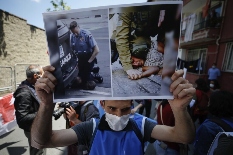 FILE - A demonstrator holds a placard with photos of George Floyd, left, a black man who died after being restrained by Minneapolis police officers on May 25, 2020 and an undated photo, right, of an Israeli soldier restraining a Palestinian youth, during a protest near the U.S. consulate in Istanbul, Thursday, June 4, 2020. (AP Photo/Emrah Gurel, File)