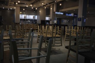 FILE - In this March 16, 2020 file photo, chairs hang stacked on empty tables at a closed restaurant in New York. Small business owners across the country waited again Wednesday, April 8, to receive loan money under the government’s $2 trillion coronavirus relief program. Despite a few reports that some companies had received their loans, the vast majority of the hundreds of thousands of owners who began applying for the loans on Friday were still in limbo. (AP Photo/Yuki Iwamura, File)