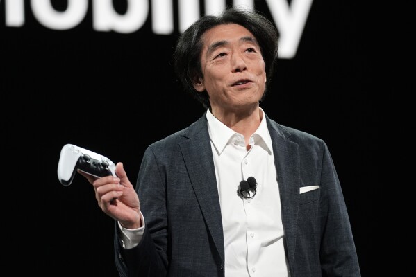 Izumi Kawanishi, president and COO of Sony Honda Mobility Inc., holds up a PlayStation controller before using it to drive an Afeela EV onto the stage during a Sony press conference ahead of the CES tech show Monday, Jan. 8, 2024, in Las Vegas. (AP Photo/John Locher)