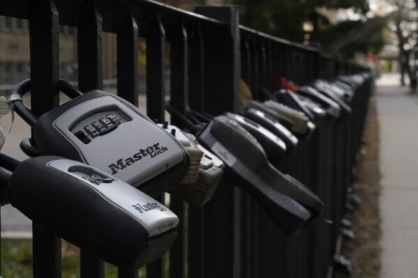 FILE - Key lock boxes for real estate showings hang on a fence outside a high-rise condominium building, Oct. 27, 2022, in Chicago. The cost of hiring a real estate agent to buy or sell a home is poised to change along with decades-old rules that have helped determine broker commissions. (AP Photo/Kiichiro Sato, File)