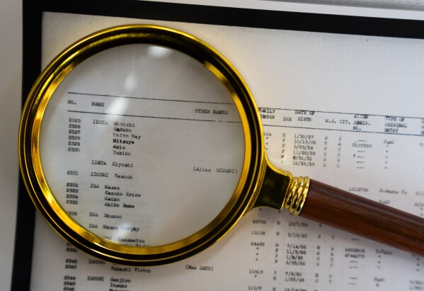 A magnifying glass sits over a page of camp records for Associated Press Photographer Lindsey Wasson's maternal grandfather Akio Ideta and family, in the visitor center at Minidoka National Historic Site, Sunday, July 9, 2023, in Jerome, Idaho. (AP Photo/Lindsey Wasson)