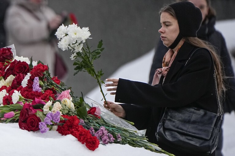 A young woman lays flowers to pay the last respect to Alexei Navalny at the monument, a large boulder from the Solovetsky islands, where the first camp of the Gulag political prison system was established, near the historical the Federal Security Service (FSB, Soviet KGB successor) building in Moscow, Russia, on Sunday, Feb. 18, 2024. Russians across the vast country streamed to ad-hoc memorials with flowers and candles to pay tribute to Alexei Navalny, the most famous Russian opposition leader and the Kremlin's fiercest critic. Russian officials reported that Navalny, 47, died in prison on Friday. (AP Photo/Alexander Zemlianichenko)