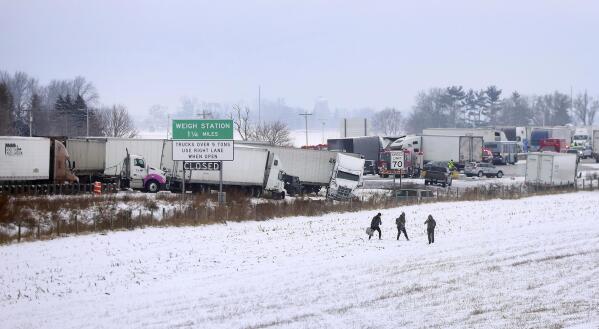 Individuals carry their belongings as they walk away as emergency crews respond to a multi-vehicle accident in both the north and south lanes of Interstate 39/90 just north of the East Creek Road overpass on Friday, Jan. 27, 2023, in Turtle, Wis. Authorities say snowy conditions led to the massive traffic pile-up in southern Wisconsin on Friday that left Interstate 39/90 blocked for hours. (Anthony Wahl/The Janesville Gazette via AP)