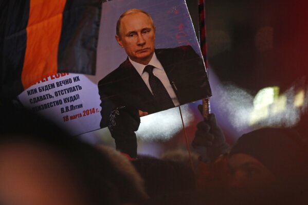 
              A person holds a banner of Russian President Vladimir Putin in Manezhnaya square, near Kremlin in Moscow, Sunday, March 18, 2018. An exit poll suggests that Vladimir Putin has handily won a fourth term as Russia's president, adding six more years in the Kremlin for the man who has led the world's largest country for all of the 21st century. (AP Photo/Pavel Golovkin)
            