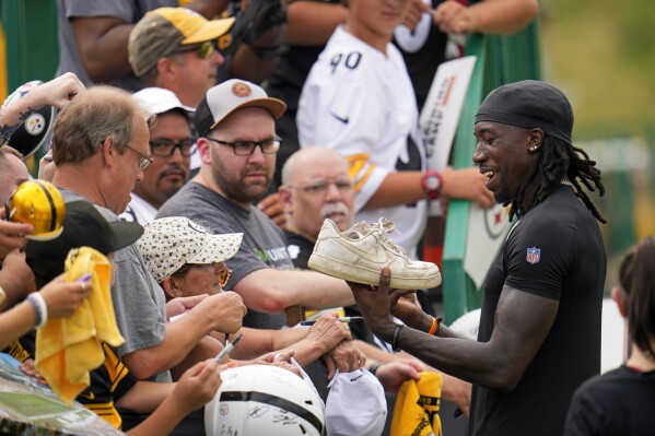 Pittsburgh Steelers cornerback Joey Porter Jr., right, laughs as a fan hands him shoe to sign following the NFL football team's training camp session in Latrobe, Pa., Thursday, July 27, 2023. (AP Photo/Gene J. Puskar)