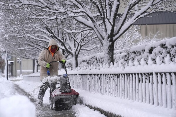 FILE - A woman shovels snow from a sidewalk in Des Moines, Iowa, Tuesday, Jan. 9, 2024.  The arctic-like temperatures that are raising concerns about voting for the Iowa caucuses on Monday, Jan. 15 are focusing attention on a presidential nominating system that has long been criticized as archaic and undemocratic.  (AP Photo/Abby Parr, File)