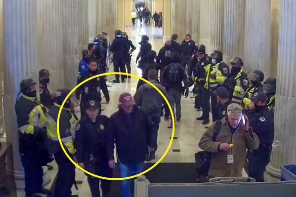 This image from U.S. Capitol Police video, contained and annotated in the Justice Department's statement of facts in support arrest warrant for Stephen Michael Baker, shows Baker, circled in yellow, being led from the U.S. Capitol on Jan. 6, 2021, in Washington, by a U.S. Capitol Police officer. Baker, a Texas-based writer for a conservative media outlet has surrendered to authorities to face charges that he joined a mob's attack on the U.S. Capitol on Jan. 6, 2021. (Department of Justice via AP)
