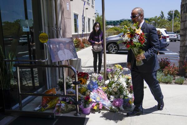 A man places flowers at a memorial honoring Dr. John Cheng sits outside his office building on Tuesday, May 17, 2022, in Aliso Viejo, Calif. Cheng, 52, was killed in Sunday's shooting at Geneva Presbyterian Church. (AP Photo/Ashley Landis)