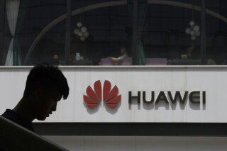 FILE - In this Thursday, May 16, 2019 file photo, a man is silhouetted near the Huawei logo in Beijing. Struggling under U.S. sanctions, Chinese tech giant Huawei has unveiled a new flagship foldable smartphone but says it will only be sold in China.  (AP Photo/Ng Han Guan, File)