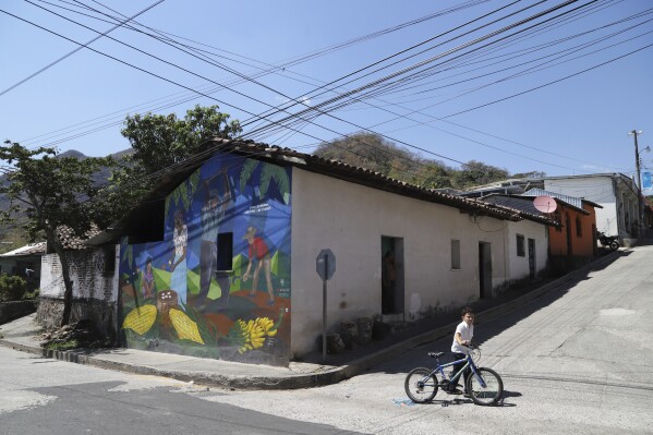 A youth pushes his bike past a mural showing farmers that reads in Spanish 