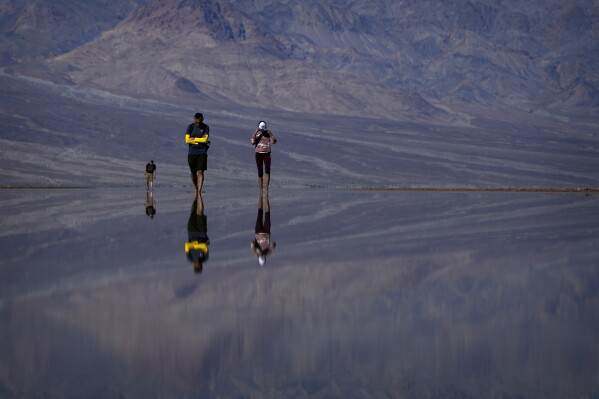 Vinaya Vijay, right, and Vijay Parthasarathy wade through water at Badwater Basin, Thursday, Feb. 22, 2024, in Death Valley National Park, Calif. The basin, normally a salt flat, has filled from rain over the past few months. (AP Photo/John Locher)