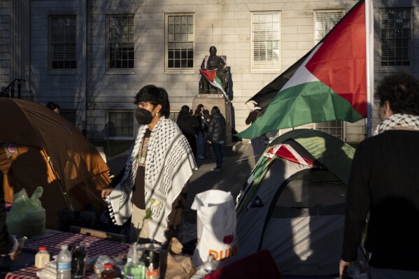 A student protester stands in front of the statue of John Harvard, the first major benefactor of Harvard College, draped in the Palestinian flag, at an encampment of students protesting against the war in Gaza, at Harvard University in Cambridge, Mass., on Thursday, April 25, 2024. (AP Photo/Ben Curtis)