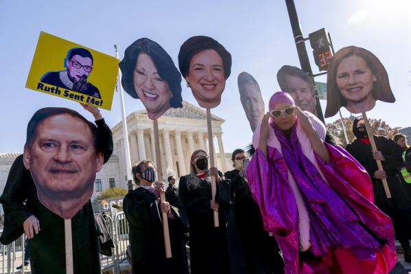 An abortion rights advocate in costume stands in front of Supreme Court justice posters as people demonstrate in front of the U.S. Supreme Court, Wednesday, Dec. 1, 2021, in Washington, as the court hears arguments in a case from Mississippi, where a 2018 law would ban abortions after 15 weeks of pregnancy, well before viability. (AP Photo/Andrew Harnik)