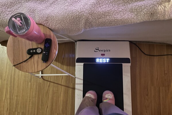 Hope Zuckerbrow, founder of the cozy cardio wellness movement, shows her workout set-up, including a walking pad, smoothie and remote control for watching television. (Hope Zuckerbrow via AP)