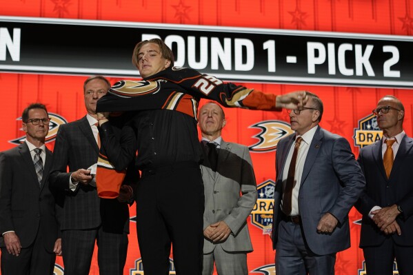 Leo Carlsson puts on an Anaheim Ducks jersey after being picked by the team during the first round of the NHL hockey draft Wednesday, June 28, 2023, in Nashville, Tenn. (AP Photo/George Walker IV)