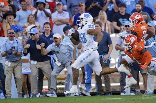 North Carolina running back Omarion Hampton (28) runs with the ball while pursued by Clemson safety Andrew Mukuba (1) and cornerback Nate Wiggins (2) during the first half of an NCAA college football game Saturday, Nov. 18, 2023, in Clemson, S.C. (AP Photo/Jacob Kupferman)