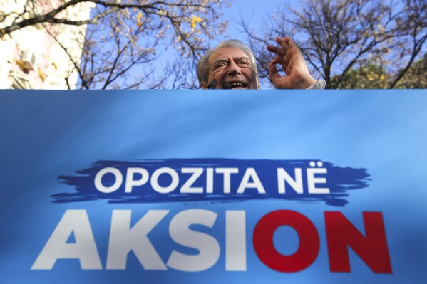 Sali Berisha, 79, the main leader of the center-right Democratic Party, delivers a speech to hundreds of protesters during an anti-government rally outside the Parliament building in Tirana, Albania, Monday, Dec. 18, 2023. Albanian opposition have protested against the government's it accuses of corruption while a parliamentary commission discusses on immunity for its leader Sali Berisha. The sign reads "Opposition in Action." (AP Photo/Armando Babani)