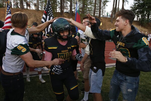 FILE - In this Aug. 23, 2019 file photo, Paradise tight end Jacob Duncan runs through a tunnel of former players during the opening ceremony of their high school football game against Williams, in Paradise, Calif.  Paradise, the  Northern California high school football team is preparing to play for a championship one year after most of the players and coaches lost their homes to a wildfire that nearly destroyed their town. Paradise High School will face Sutter Union High School on Saturday, Nov. 30  for the Northern Section Division III championship.(AP Photo/Rich Pedroncelli, File)