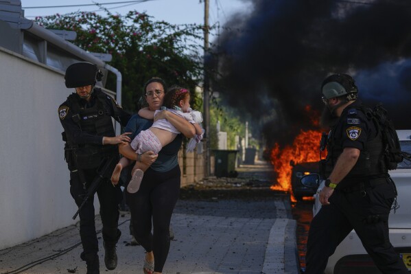 Police officers evacuate a woman and a child from a site hit by a rocket fired from the Gaza Strip in Ashkelon, southern Israel, Saturday, Oct. 7, 2023. (AP Photo/Tsafrir Abayov)