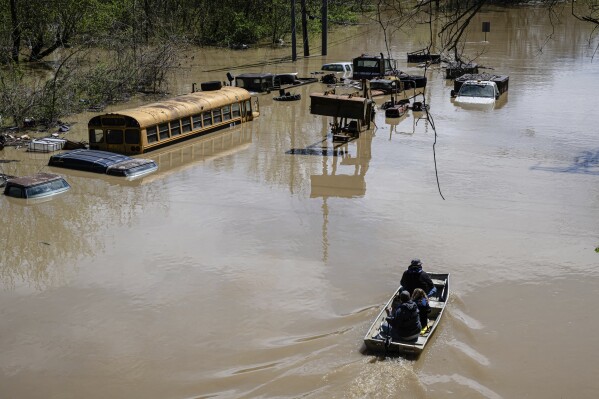 Community members steer a boat past flooded vehicles on Monday, April 7, 2025, in Frankfort, Ky. (AP Photo/Jon Cherry)