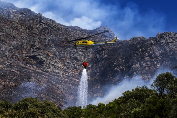 A fire fighting helicopter battles a vegetation fire on the slopes above Simon's Town, around 40 kilometres (25 miles) south of Cape Town, South Africa, Tuesday, Dec. 19, 2023. More than 300 firefighters were battling a blaze on the slopes of a mountain near Cape Town in South Africa for a second day on Wednesday and residents were evacuated from at least one neighbourhood overnight, emergency services said. (AP Photo)