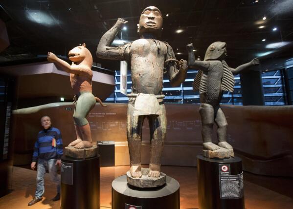 FILE- A visitor looks at wooden royal statues of the Dahomey kingdom, dated 19th century, at the Quai Branly museum in Paris, France, Nov. 23, 2018. African countries’ efforts at restitution of artifacts from institutions in Europe are now blossoming with the return of pieces that once were thought unattainable. But many objects are still out of reach, and some officials worry they don't even know the true extent of what was taken abroad. (AP Photo/Michel Euler, File)