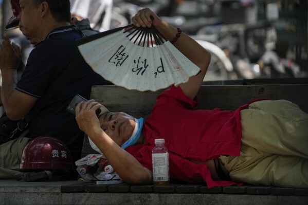 FILE - A man cools himself with a fan while browsing his phone on a sweltering day in Beijing, July 16, 2023. A new study Tuesday, July 25, finds increase in heat-trapping gases, has made heat waves more common— the one in China — 50 times more likely. (AP Photo/Andy Wong, File)