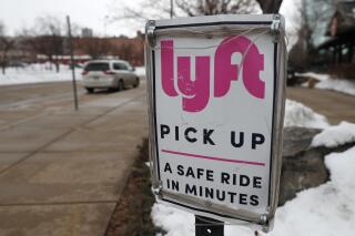 FILE -In this Wednesday, Feb. 12, 2020, photo, a sign marks the pick lane for Lyft car share service outside the Pepsi Center in downtown Denver.  Ford Motor Co. and a self-driving vehicle company it partly owns will join with the Lyft ride-hailing service to offer autonomous rides on the Lyft network. The service using Ford vehicles and a driving system developed by Argo AI will begin in Miami later this year and start in Austin, Texas, in 2022.  (AP Photo/David Zalubowski)