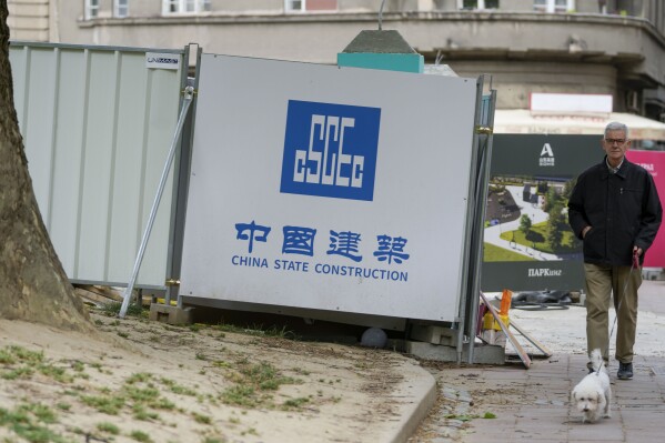 A man with a dog walks by a construction site in Belgrade, Serbia, Wednesday, May 1, 2024. Chinese President Xi Jinping will visit France, Serbia and Hungary next week as Beijing appears to seek a larger role in the conflict between Russia and Ukraine that has upended global political and economic security. (AP Photo/Darko Vojinovic)