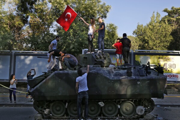 FILE -Turkish citizens stand on a damaged Turkish military APC that was attacked by protesters in a street near the Turkish military headquarters in Ankara, Turkey, July 16, 2016. (AP Photo/Hussein Malla, File)