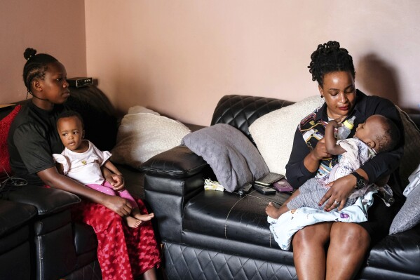 Caroline lkendi, right, feeds her twin son Creflo Curtis with formula milk as nanny, Hadijja, left, carries her other son Roylty Curtis at lkendi's home in Kampala, Uganda, Tuesday, May 21, 2024. ATTA Breastmilk Community was launched in 2021, by a woman who had struggled like Ikendi without getting support. The registered nonprofit, backed by grants from organizations and individuals, is the only group outside a hospital setting in Uganda that conserves breast milk in substantial amounts. (AP Photo/Hajarah Nalwadda)