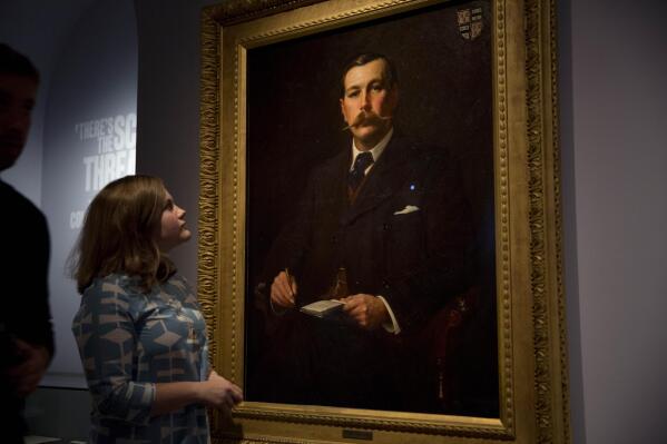 FILE - A Museum of London employee poses for photographers next to an 1897 oil on canvas portrait of Sherlock Holmes author Sir Arthur Conan Doyle by illustrator Sidney Paget on display as part of the exhibition "Sherlock Holmes: The Man Who Never Lived and Will Never Die" at the Museum of London in London, Oct. 16, 2014. Sherlock Holmes is finally free to the public in 2023. The long dispute on contested copyright on Doyle's tales of a whip-smart detective will come to an end in 2022, as the final Sherlock Holmes stories by Doyle will be released on Saturday, Dec. 31, as copyrights from 1927 expire on Jan. 1, 2023. (AP Photo/Matt Dunham, File)