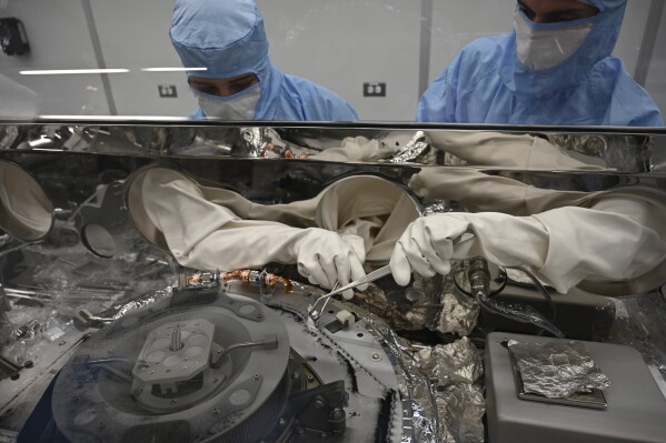 FILE - In this photo provided by NASA, Mari Montoya, left, and Curtis Calva use tools to collect asteroid particles from the base of a canister on Sept. 27, 2023, at Johnson Space Center in Houston. The Osiris-Rex spacecraft delivered a batch of rubble collected from the asteroid Bennu. (NASA via AP, File)