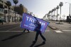 ARQUIVO - Uma mulher atravessa a rua com uma bandeira em apoio ao presidente Donald Trump durante um comício em Huntington Beach, Califórnia, 6 de janeiro de 2021.  Uma mudança nas regras estaduais do Partido Republicano abriu a possibilidade de varrer todo o comício da Califórnia.  Delegados nas eleições primárias de 5 de março, o prêmio mais gordo na disputa de indicação do partido.  A eleição acontece na Superterça, quando a Califórnia está entre mais de uma dúzia de estados que realizam primárias.  (Foto AP / Jay C. Hong, Arquivo)