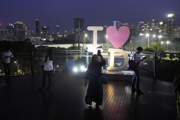 A woman uses her mobile phone to take video of the city skyline at a shopping mall in Jakarta, Indonesia, Wednesday, Jan. 11, 2023. Population and economic growth in Indonesia are expected to triple the country's energy consumption by 2050. (AP Photo/Dita Alangkara)