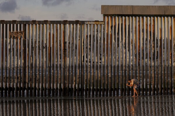 A man takes an image with his phone next to where the border wall separating Mexico and the United States reaches the Pacific Ocean Tuesday, Jan. 28, 2025, in Tijuana, Mexico. (AP Photo/Gregory Bull)