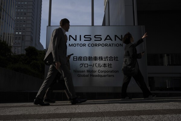 Visitors walk past Nissan signage at Nissan headquarters in Yokohama, Tuesday, May 13, 2025. (AP Photo/Louise Delmotte)