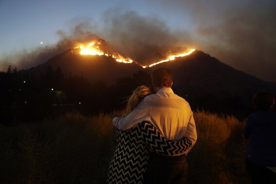 Roger Bloxberg, right, and his wife Anne hug as they watch a wildfire on a hill top near their home Friday, Nov. 9, 2018, in West Hills, Calif. (AP Photo/Marcio Jose Sanchez, File)