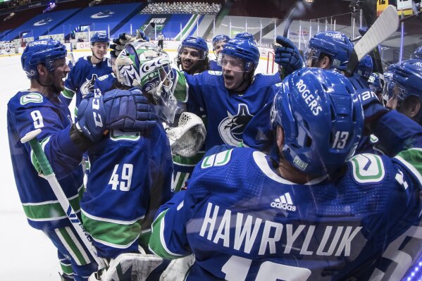 Vancouver Canucks' J.T. Miller (9), goalie Braden Holtby (49) and Brock Boeser (6) celebrate with teammates after the winning goal during overtime of an NHL hockey game against the Toronto Maple Leafs in Vancouver, British Columbia, Sunday, April 18, 2021. (Darryl Dyck/The Canadian Press via AP)