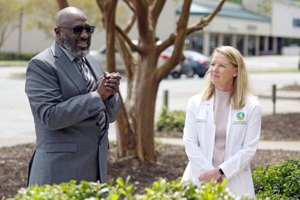 Dr Michael McDuffie, CEO Agape Heath Services of Eastern North Carolina, left, speaks during a ribbon cutting ceremony outside the clinic with Kristen Warren, at right, in Williamston, N.C., Wednesday, April 10, 2024. After Martin General closed, the city's only hospital, residents there say they're not only worried about their health but they've lost trust in politicians. The struggle to reopen its only emergency room could signal trouble for President Joe Biden's re-election campaign, which is centered around his health care accomplishments. McDuffie wants to reopen Martin General, even if just as a stand-alone emergency room. (AP Photo/Karl B DeBlaker)