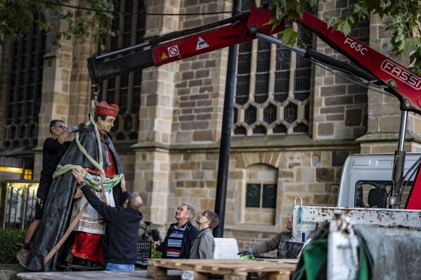The sculpture of Essen Cardinal Franz Hengsbach hangs on a crane in front of Essen Cathedral after being dismantled and loaded onto a truck in Essen, Germany, Monday Sept. 25, 2023. A statue of a deceased German cardinal was removed from its perch outside Essen Cathedral in western Germany on Monday, days after allegations of sexual abuse decades ago became public. (Christoph Reichwein/dpa via AP)