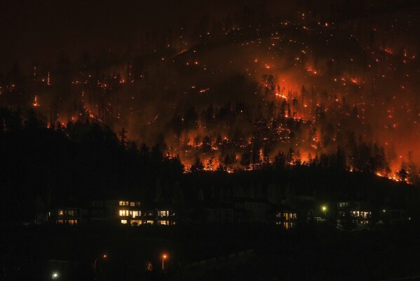 FILE - The McDougall Creek wildfire burns on the mountainside above houses in West Kelowna, British Columbia, on Aug. 18, 2023. Wildfires are bringing fresh scrutiny to Canada's fossil fuel dominance, its environmentally friendly image and the viability of becoming carbon neutral by 2050.(Darryl Dyck/The Canadian Press via AP, File)