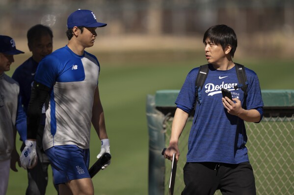 FILE - Los Angeles Dodgers' Shohei Ohtani walks with interpreter Ippei Mizuhara at batting practice during spring training baseball workouts in Phoenix on Feb. 12, 2024. The former longtime interpreter for Los Angeles Dodgers star Shohei Ohtani has been charged with federal bank fraud for crimes involving gambling debts and theft of millions of dollars from the slugger. Federal authorities announced the development Thursday, April 11, at a press conference in Los Angeles. (AP Photo/Carolyn Kaster, File)