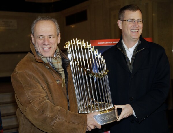 FILE -FILE - Boston Red Sox CEO Larry Lucchino, left, and Chief Operating Officer Sam Kennedy hold the 2013 World Series baseball trophy on the red carpet at the Wang Theatre before a screening of a DVD about the series in Boston., Nov. 23, 2013. Larry Lucchino, the force behind baseball's retro ballpark revolution and the transformation of the Boston Red Sox from cursed losers to World Series champions, has died. He was 78. Lucchino had suffered from cancer. The Triple-A Worcester Red Sox, his last project in a career that also included three major league baseball franchises and one in the NFL, confirmed his death on Tuesday, April 2, 2024. (AP Photo/Steven Senne, File)