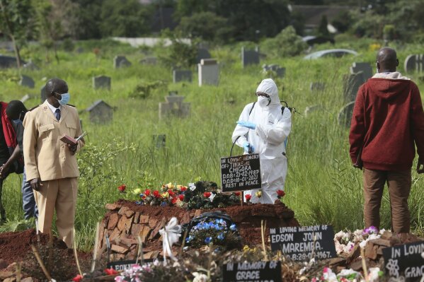 A preacher speaks to a health worker, during a burial of a person who died from COVID-19, in Harare, Friday, Jan, 15, 2021. Zimbabwe, battling a spike in new COVID-19 cases, has banned families from transporting their dead relatives between cities, as part of new measures to stop traditional funeral rites that are believed to be increasing the spread of the disease. (AP Photo/Tsvangirayi Mukwazhi)