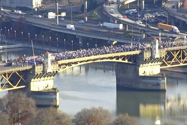 In this KGW-TV image from video, striking teachers march across the Burnside Bridge in Portland, Ore., on Tuesday, Nov. 21, 2023. KGW reported that the Portland Association of Teachers union and their supporters stopped in the middle of the bridge for about 15 minutes. Portland teachers have been on strike since Nov. 1, with class sizes and teacher salaries are among the key issues the union and the school district have been negotiating. (KGW-TV via AP)